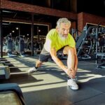 Warming up. Portrait of athletic middle aged man in sportswear stretching legs before training in